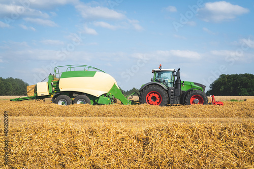 Strohernte - Traktor mit moderner Hochdruckpresse beim Pressen von Strohballen in Quaderform.