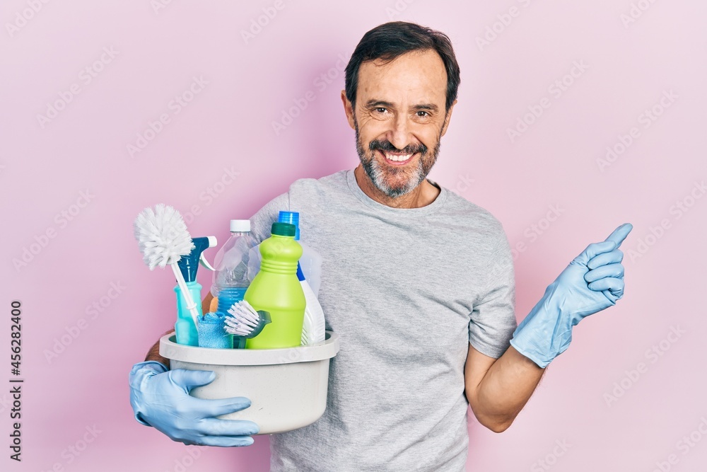 Middle age hispanic man holding cleaning products smiling happy pointing with hand and finger to the side Middle age hispanic man holding cleaning products smiling happy pointing with hand and finger to the side