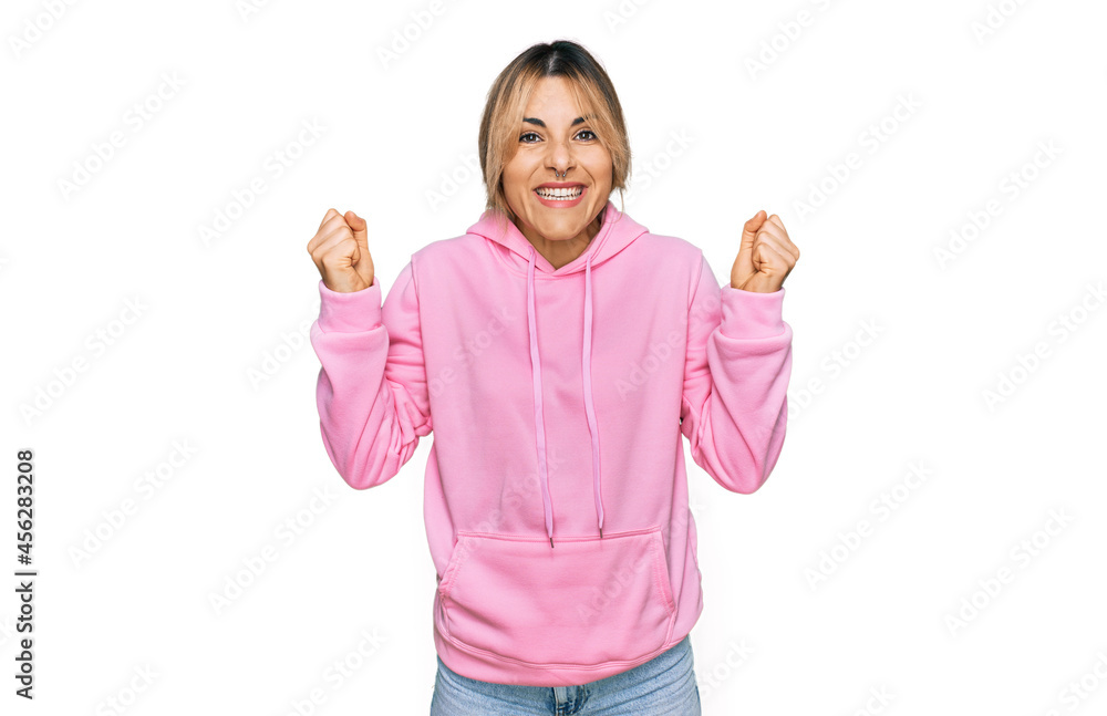 Young caucasian woman wearing casual sweatshirt celebrating surprised and amazed for success with arms raised and open eyes. winner concept. Young caucasian woman wearing casual sweatshirt celebrating surprised and amazed for success with arms raised and open eyes. winner concept.