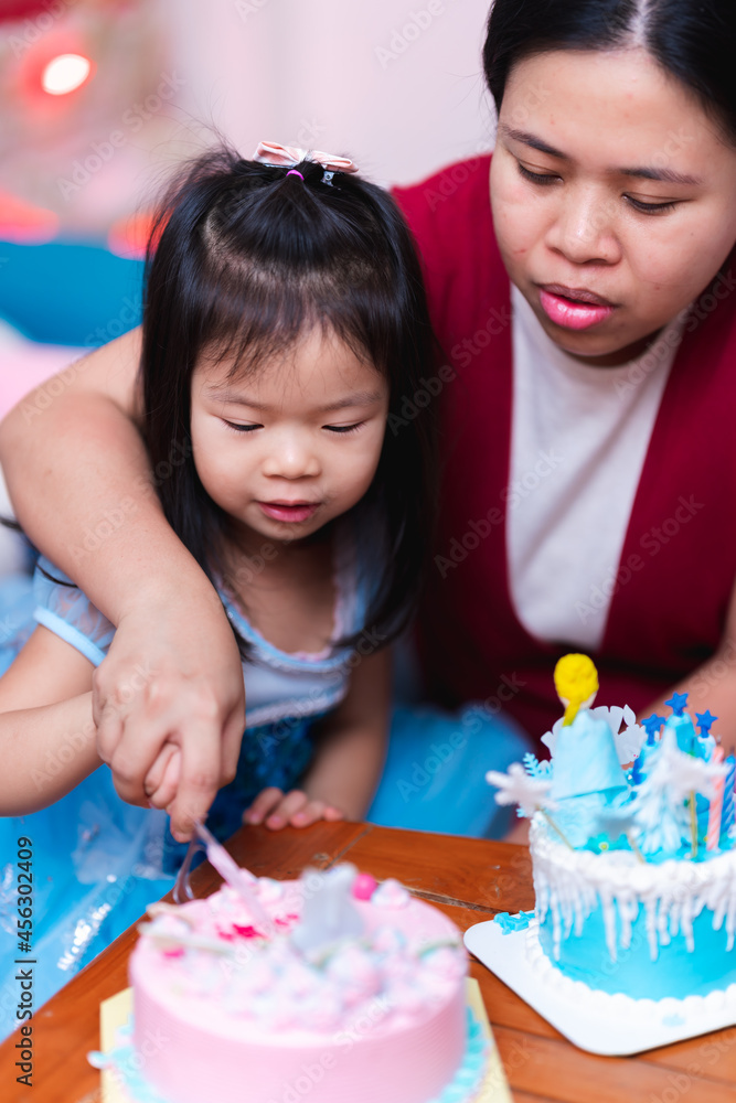 Asian family is hosting a birthday party for little daughter. Mother and daughter cut the pink cake after blowing out the candles. Little girl was wearing blue princess dress. Child are 4 years old. Asian family is hosting a birthday party for little daughter. Mother and daughter cut the pink cake after blowing out the candles. Little girl was wearing blue princess dress. Child are 4 years old.