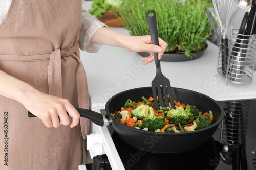 Fényképezés Woman frying vegetables on stove in kitchen