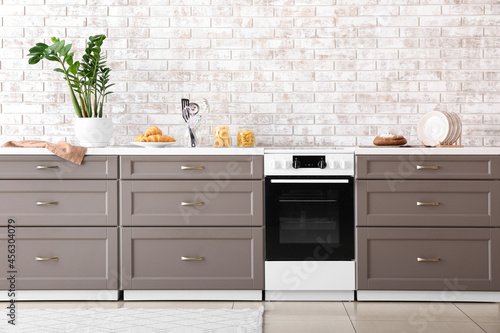 Modern furniture with electric oven near brick wall