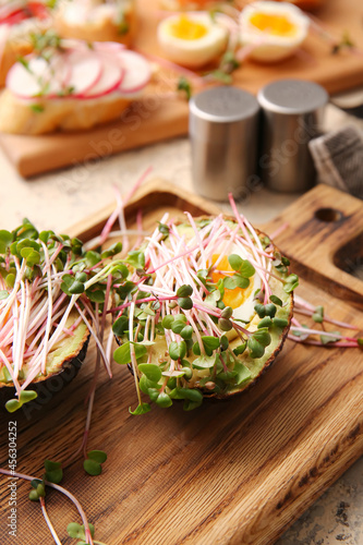 Wooden board with stuffed avocado and micro green on table, closeup