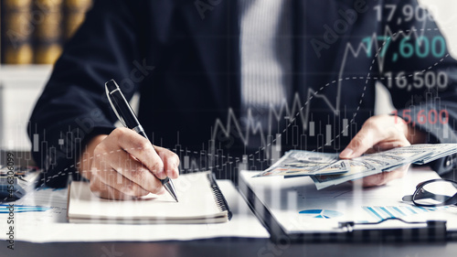 close up of businesswomen counting dollar banknote at the workplace, stock market or forex trading graph board candlestick chart, paperwork, cash flow, economic, investment, and financial concept.