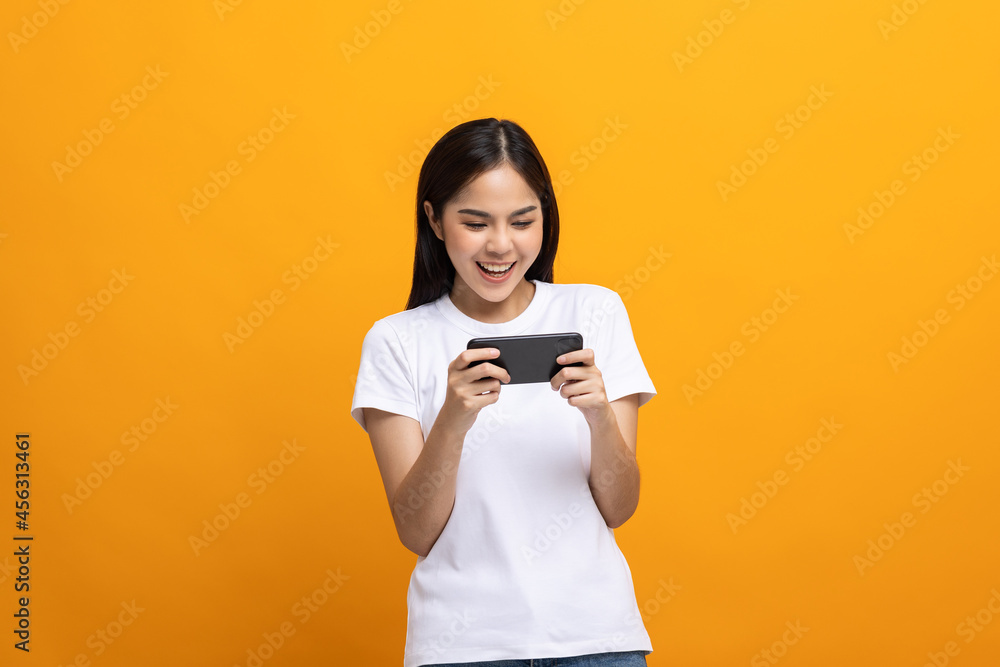 Excited Beautiful young asian women play mobile game and standing on isolated yellow background. Playing game on smartphone winning victory moment. Very enjoy and fun relax time Excited Beautiful young asian women play mobile game and standing on isolated yellow background. Playing game on smartphone winning victory moment. Very enjoy and fun relax time