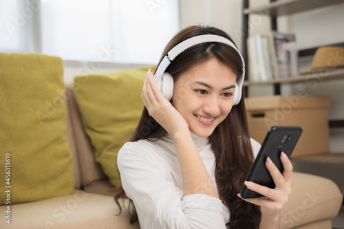 Relaxing time in living room. Beautiful young asian woman choose music from smartphone take a rest and listening song with headphone and dancing. Lifestyle in living room at house in the morning.