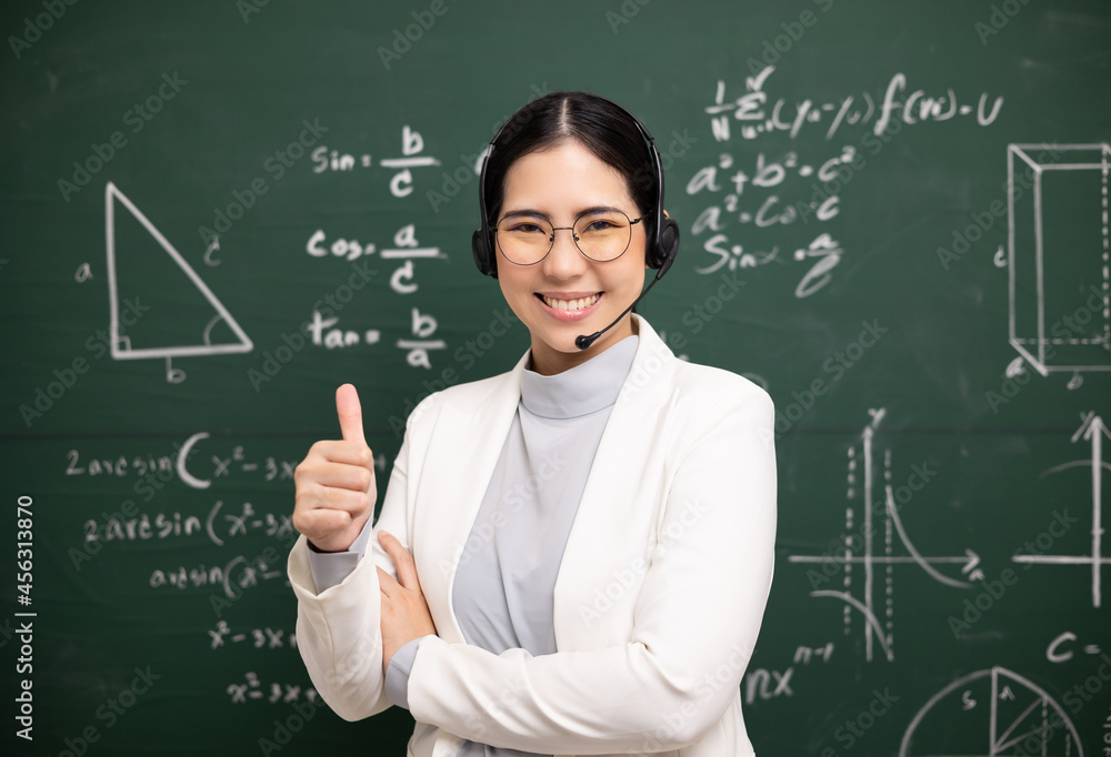 Young asian teacher woman teaching showing thumbs up and video conference with student looking camera. Female teacher training the mathematics in classroom blackboard from online course.