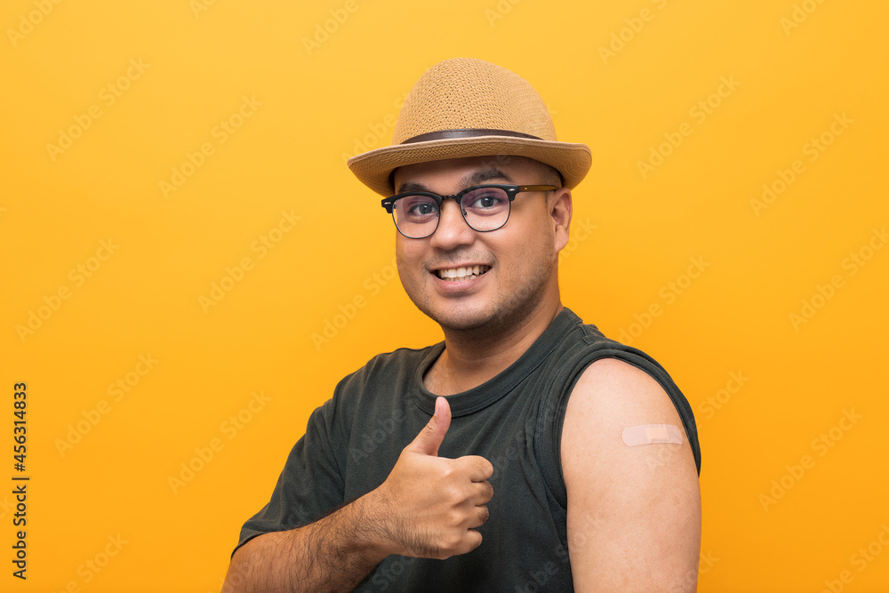 Vaccinated asian man with hat showing arm after coronavirus Vaccination isolated yellow Background. Indian man getting a vaccination covid-19 immunization Vaccinated asian man with hat showing arm after coronavirus Vaccination isolated yellow Background. Indian man getting a vaccination covid-19 immunization