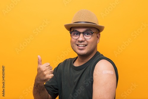 Vaccinated asian man with hat showing arm after coronavirus Vaccination isolated yellow Background. Indian man getting a vaccination covid-19 immunization