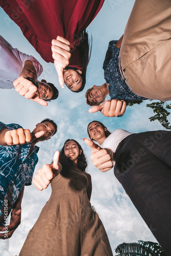 Six young friends gather together and give a thumbs up. Shot from the ground looking up. Successful teamwork concept. photo