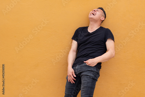 Man against yellow wall. Latin man laughing loudly wearing a black shirt. Natural laughter and belly laugh. Concept of expressions with copy space on single color background.