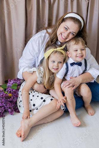 Portrait of a happy young European woman sitting on the floor with her son and daughter and hugging them. Happy blonde children feel the love of their mother. Lifestyle, space for text. High quality