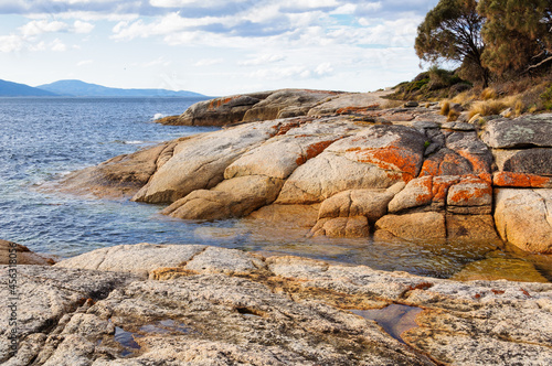 Granite boulders reddened by lichens are polished smooth by waves - Swansea, Tasmania, Australia © lkonya