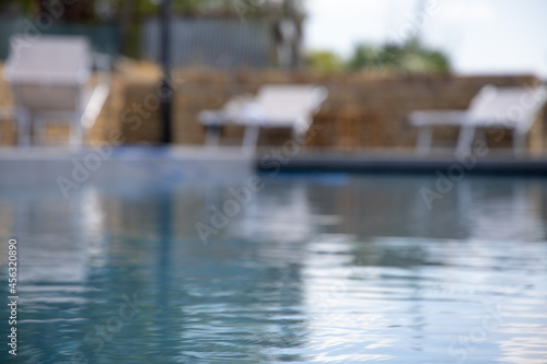 Blurred image of swimming pool with sunbathing chairs. Summertime resort background. 