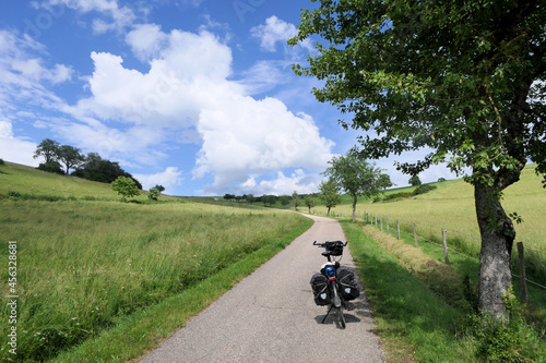 Summer feeling, a bike with panniers stands in the midday sun on a lonely road between two hilly meadows.