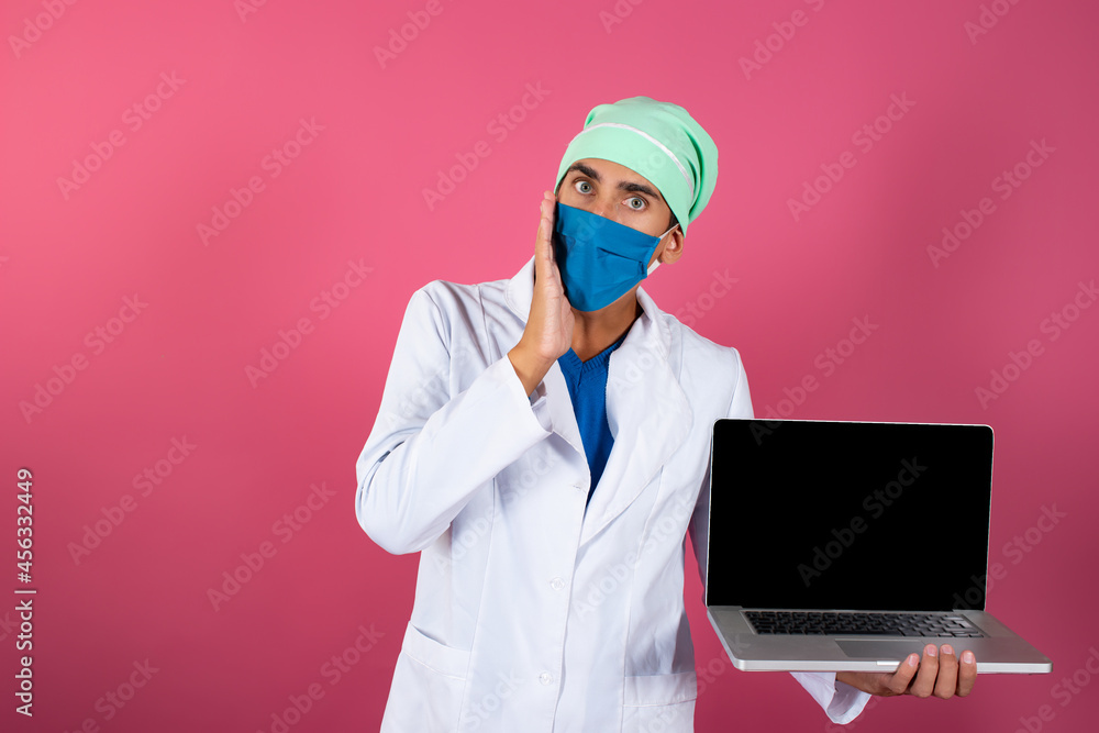 A young and handsome doctor with a laptop in his hands on a pink background. Online consultation of a medical professional. A young and handsome doctor with a laptop in his hands on a pink background. Online consultation of a medical professional.