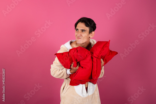 Funny cute man in pajamas and red pillows. Preparing for sleep. Pink background.