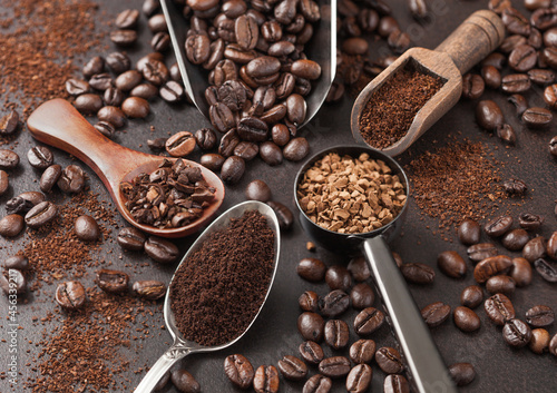 Various scoops with ground and bean coffee and freeze dried instant coffee granules on brown background.