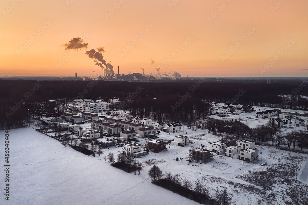 Drone image from a residential area covered with snow and industrial factory during sunset in Germany