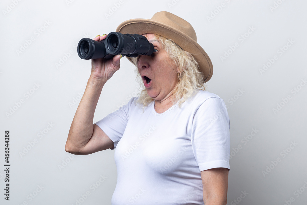Surprised old woman holding binoculars on a light background Surprised old woman holding binoculars on a light background