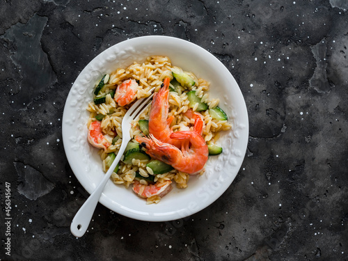 Delicious mediterranean lunch - creamy orzotto with shrimp and zucchini on a dark background, top view