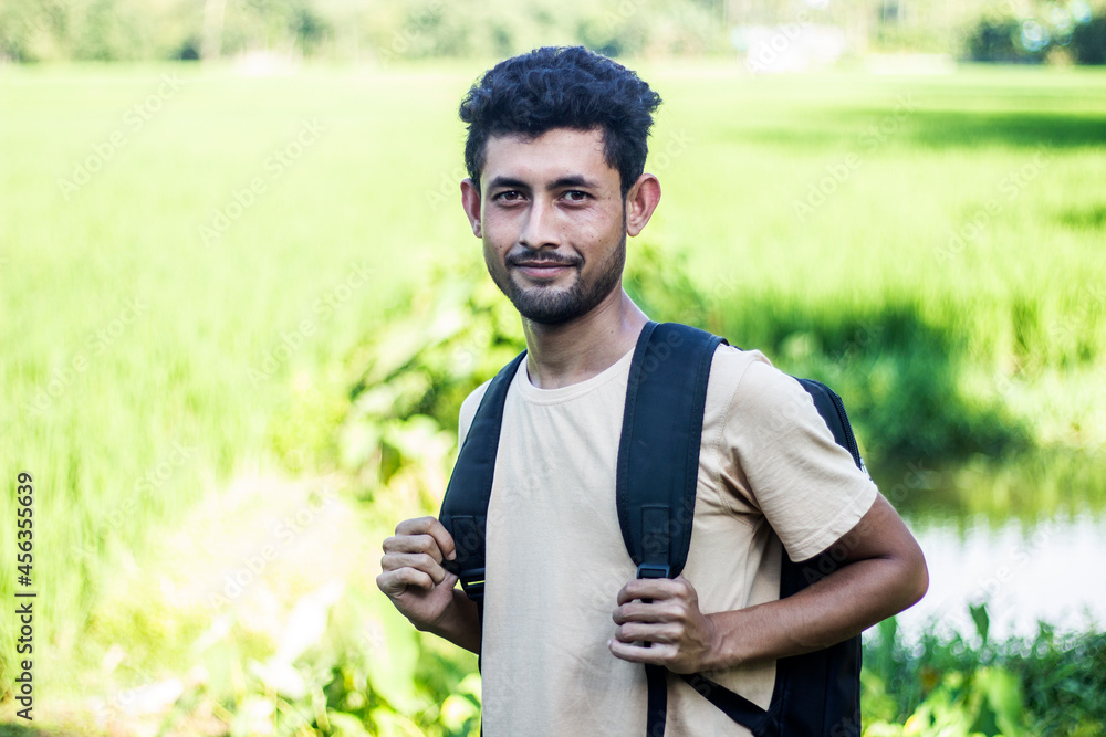 A handsome boy is standing with a black bag around his neck wearing a brown T-shirt and smile. His behind the background blur. A handsome boy is standing with a black bag around his neck wearing a brown T-shirt and smile. His behind the background blur.