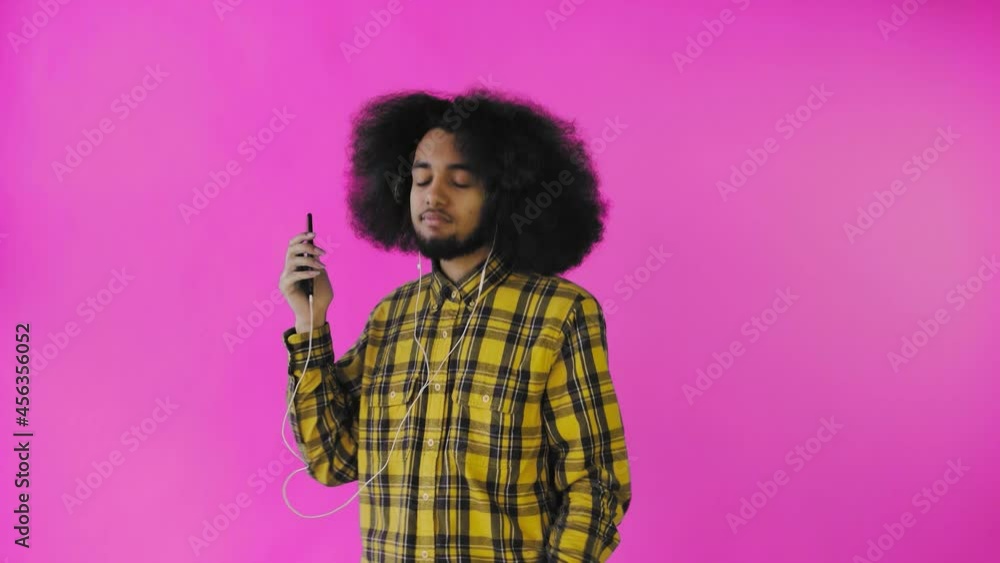A young man with an African hairstyle on a pink background is listening to music and headphones . On a colored background A young man with an African hairstyle on a pink background is listening to music and headphones . On a colored background