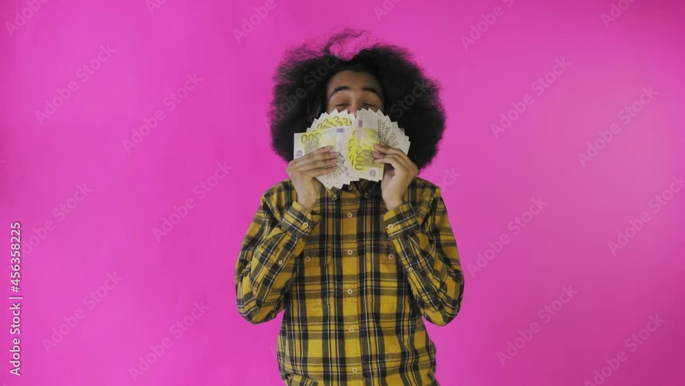 A happy African-American man holding a fan of banknotes in his hands and looking at the camera, standing isolated on a pink background A happy African-American man holding a fan of banknotes in his hands and looking at the camera, standing isolated on a pink background