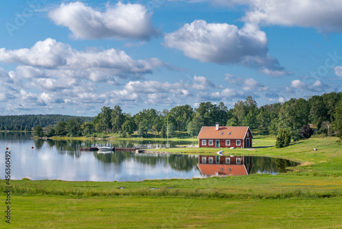 Typical red wooden house in countryside by the sea in natire of southern Sweden on a beautiful sunny summer day. Relaxing rural landscape. Reflection on water surface. Holiday in Sweden. photo