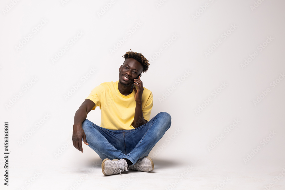 Portrait of a smiling afro american man sitting on the floor talking on the phone isolated on a white background Portrait of a smiling afro american man sitting on the floor talking on the phone isolated on a white background