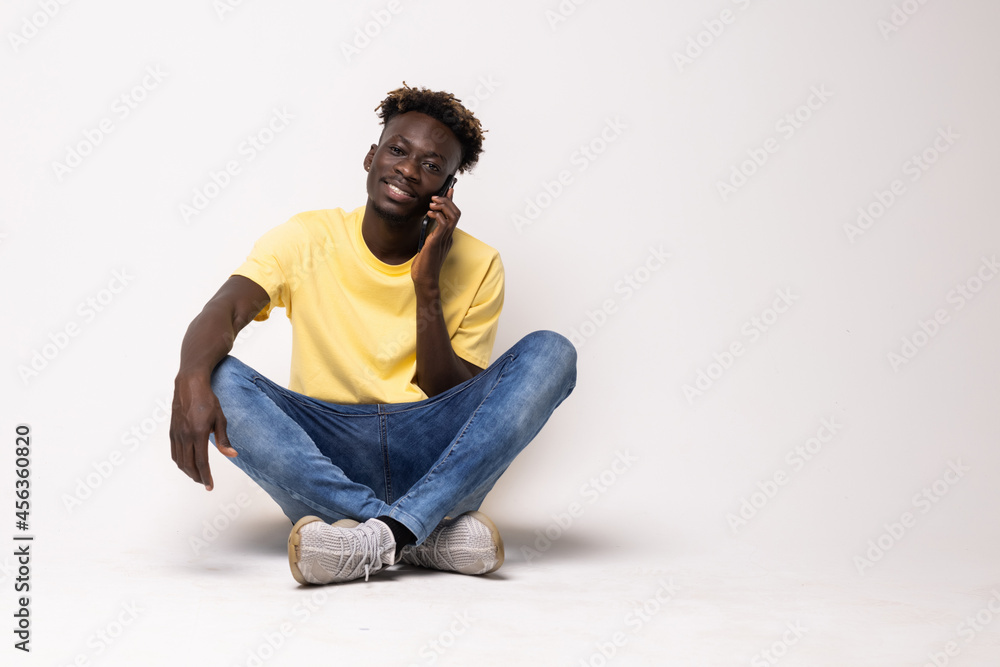 Portrait of a smiling afro american man sitting on the floor talking on the phone isolated on a white background Portrait of a smiling afro american man sitting on the floor talking on the phone isolated on a white background