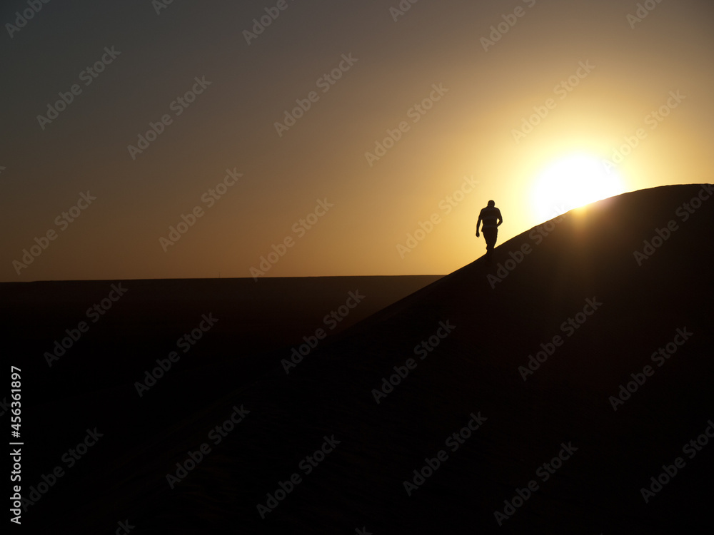 Man silhouette walking in sand dune at sunset
