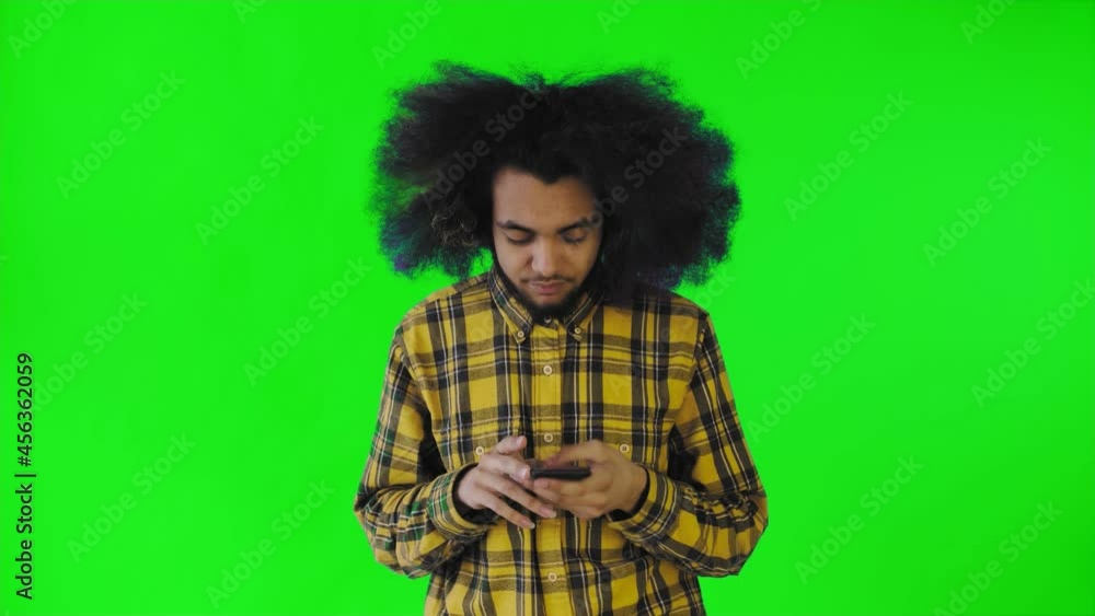 A young man with an African hairstyle on a green background pulls out his phone, but it doesn't work. Emotions on a colored background A young man with an African hairstyle on a green background pulls out his phone, but it doesn't work. Emotions on a colored background