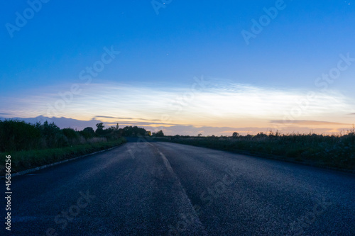 A country road heading into the distance. With the glow of Noctilucent clouds in the morning sky