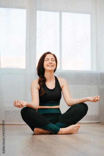 Young athlete sitting in the lotus position is sitting on the floor in an apartment. Concept relaxation and yoga.