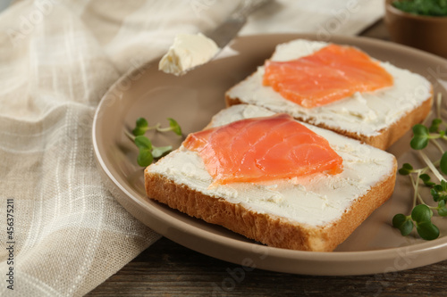 Delicious sandwiches with cream cheese and salmon on wooden table, closeup