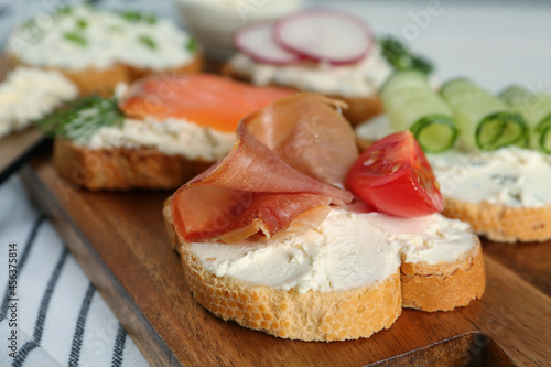 Toasted bread with cream cheese and different toppings on wooden board, closeup