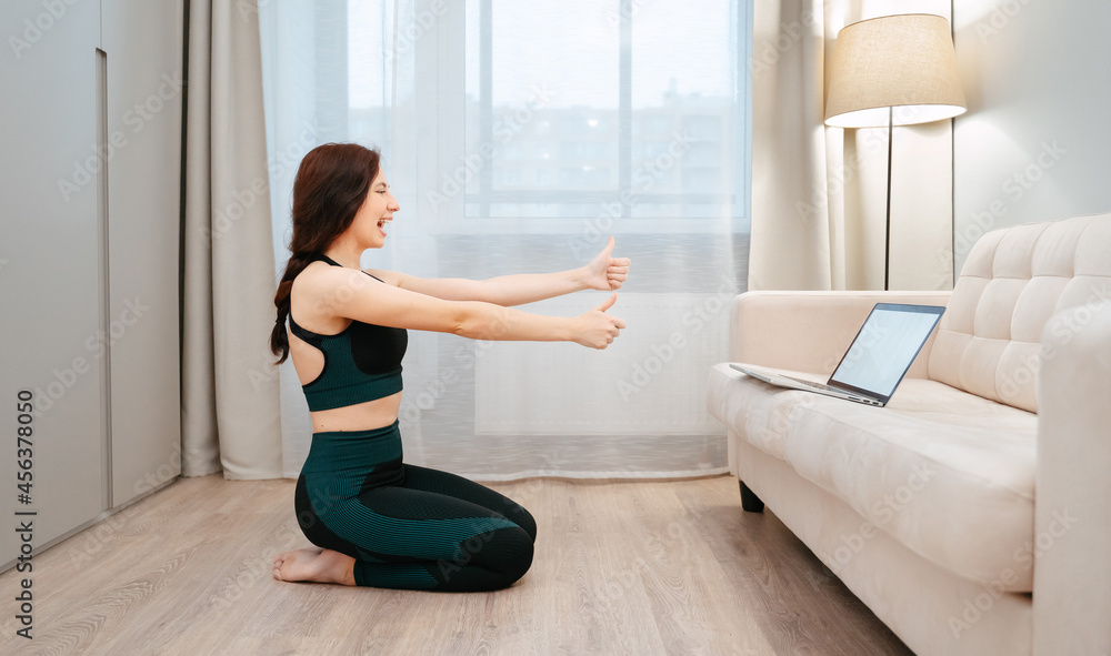 Sporty woman is happy with doing online yoga with a laptop in the living room of the house.Fitness and healthy lifestyle Sporty woman is happy with doing online yoga with a laptop in the living room of the house.Fitness and healthy lifestyle