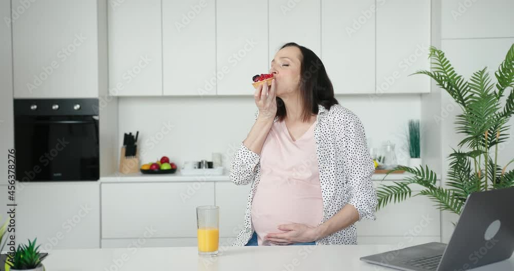 Positive pregnant woman eats tart with berries in kitchen Positive pregnant woman eats tart with berries in kitchen