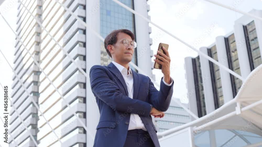 Asian confidently business man in glasses and suit talking on mobile phone outdoor in city. Asian confidently business man in glasses and suit talking on mobile phone outdoor in city.