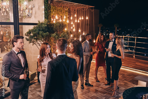 Group of people in formalwear communicating and smiling while spending time on luxury party