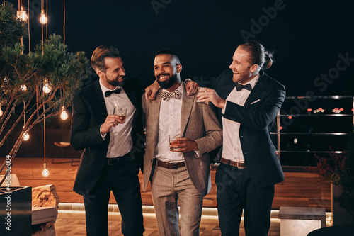 Canvas Print Three handsome men in suits drinking whiskey and communicating while spending ti