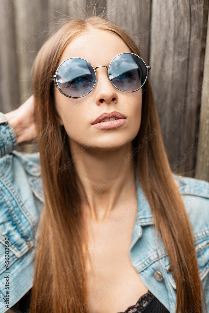 Cool portrait of a young woman with fashion blue sunglasses in a stylish denim jacket outdoors Cool portrait of a young woman with fashion blue sunglasses in a stylish denim jacket outdoors