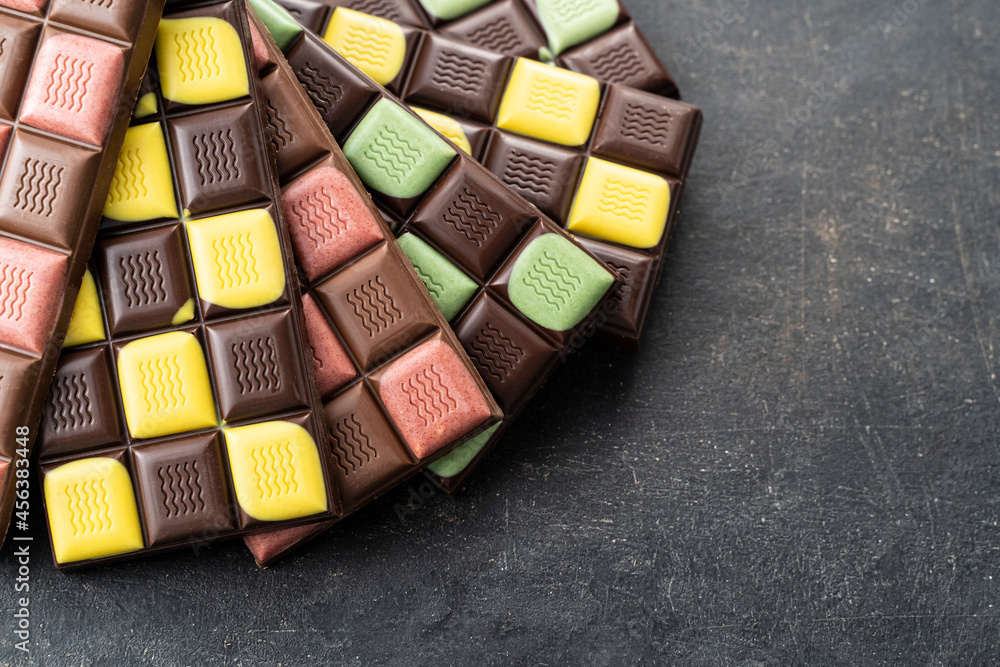 Fototapeta premium Multicolored fruit chocolate bars on black background. Handmade chocolate with mint, mango, orange, strawberry flavor. Healthy food concept, delicious chocolate sweets for kids, diet, sugar