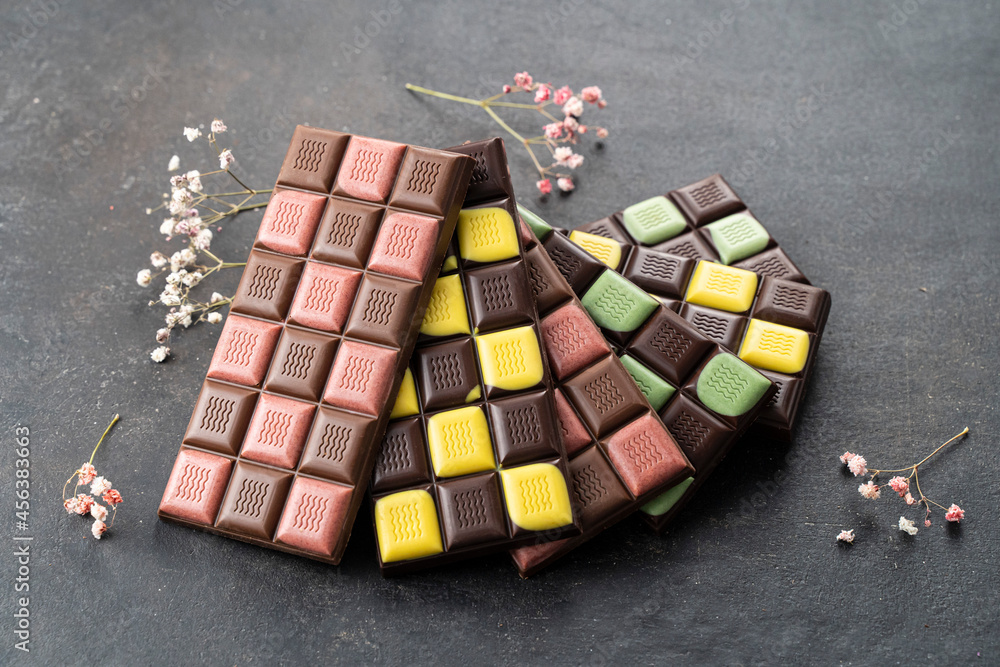 Multicolored fruit chocolate bars on black background. Handmade chocolate with mint, mango, orange, strawberry flavor. Healthy food concept, delicious chocolate sweets for kids, diet, sugar