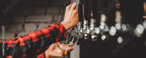 Photography bartender woman's hand holds a glass and pours light craft beer from the tap