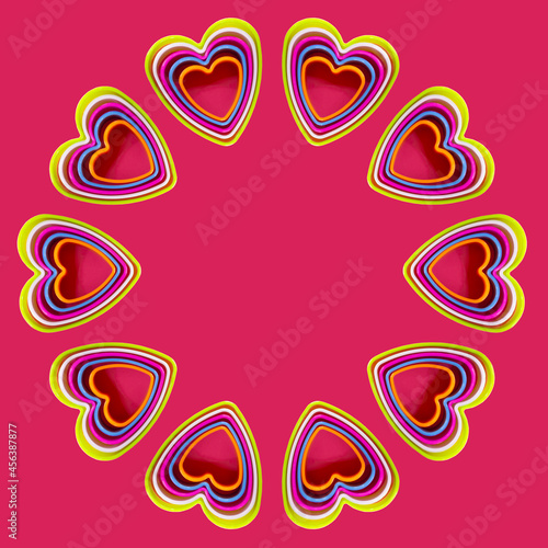 Round frame of colorful heart shaped cookie cutters on pink background, flat lay.