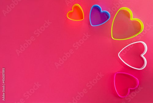 Multi-colored heart shaped cookie cutters over a pink background.