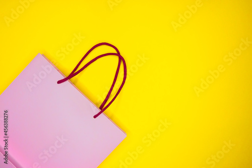 Pink paper shopping bag on yellow background. Black Friday sale shopping.