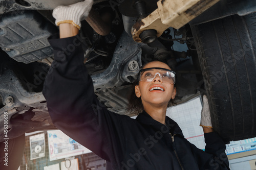 Female auto mechanic workin garage, car service technician woman check and repair customer’s car at automobile service center, inspect car under bod and suspension system, vehicle repair service shop.